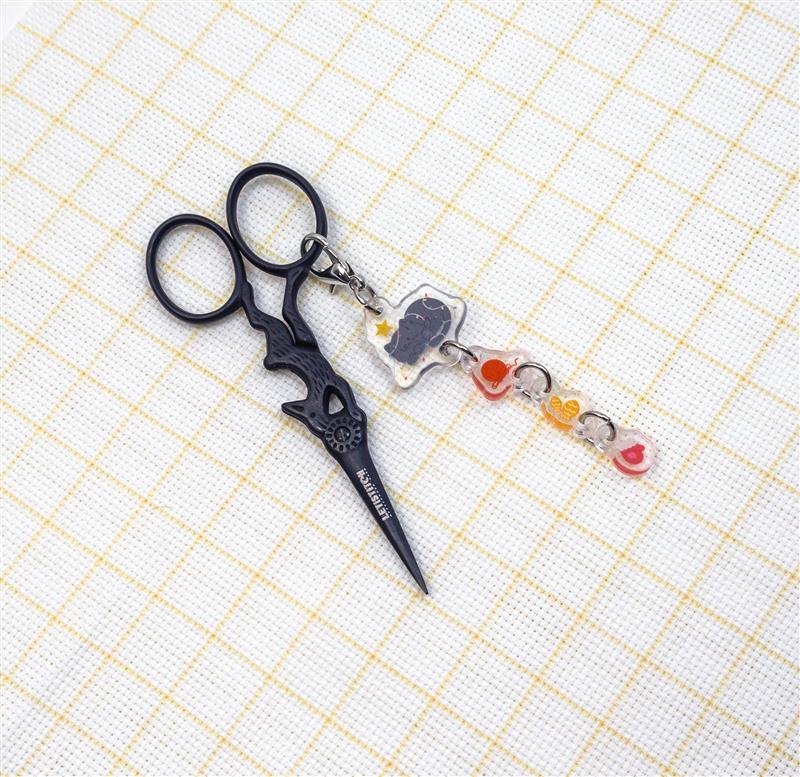 Black scissors keychain with colorful charms on a grid background