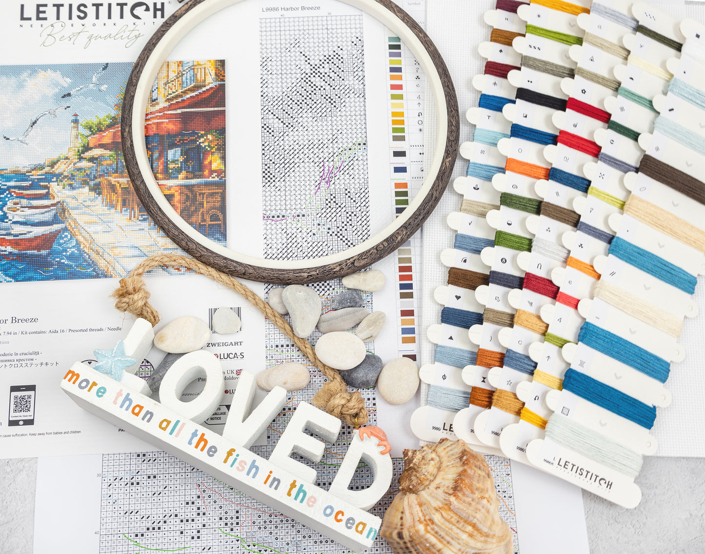 Embroidery hoop, cross-stitch pattern, thread colors, and decorative elements on a table.