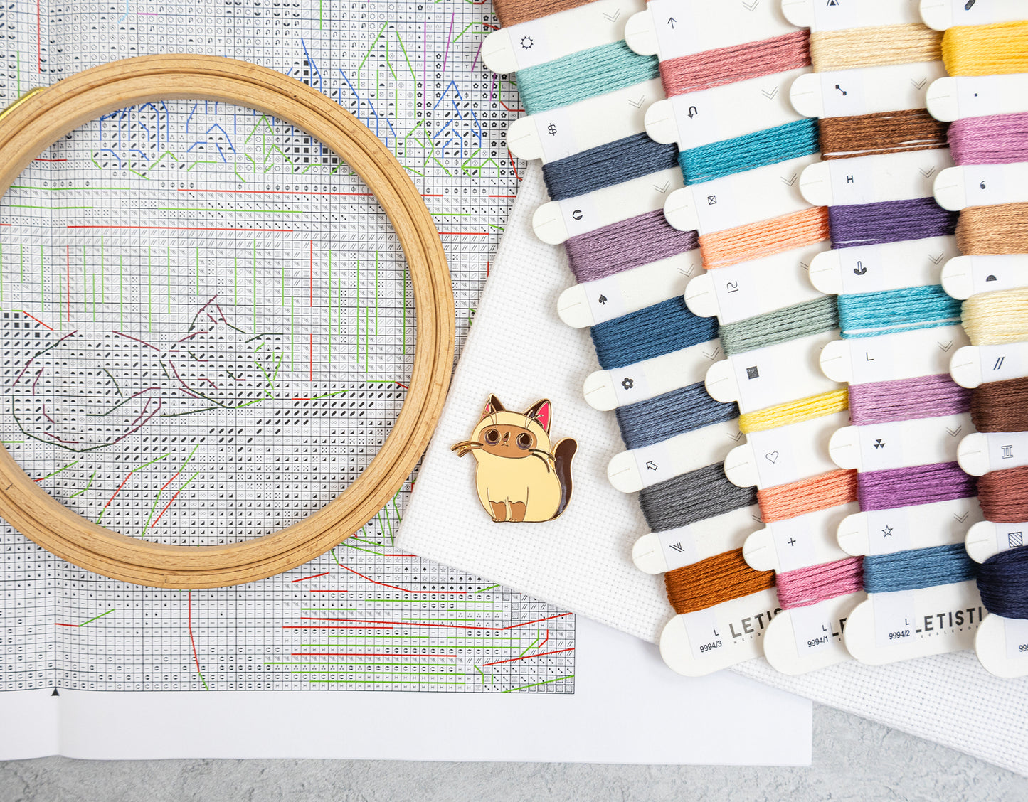 Card filled with many small thread or embroidery floss swatches in assorted colors, photographed on a light gray textured surface with a magnet