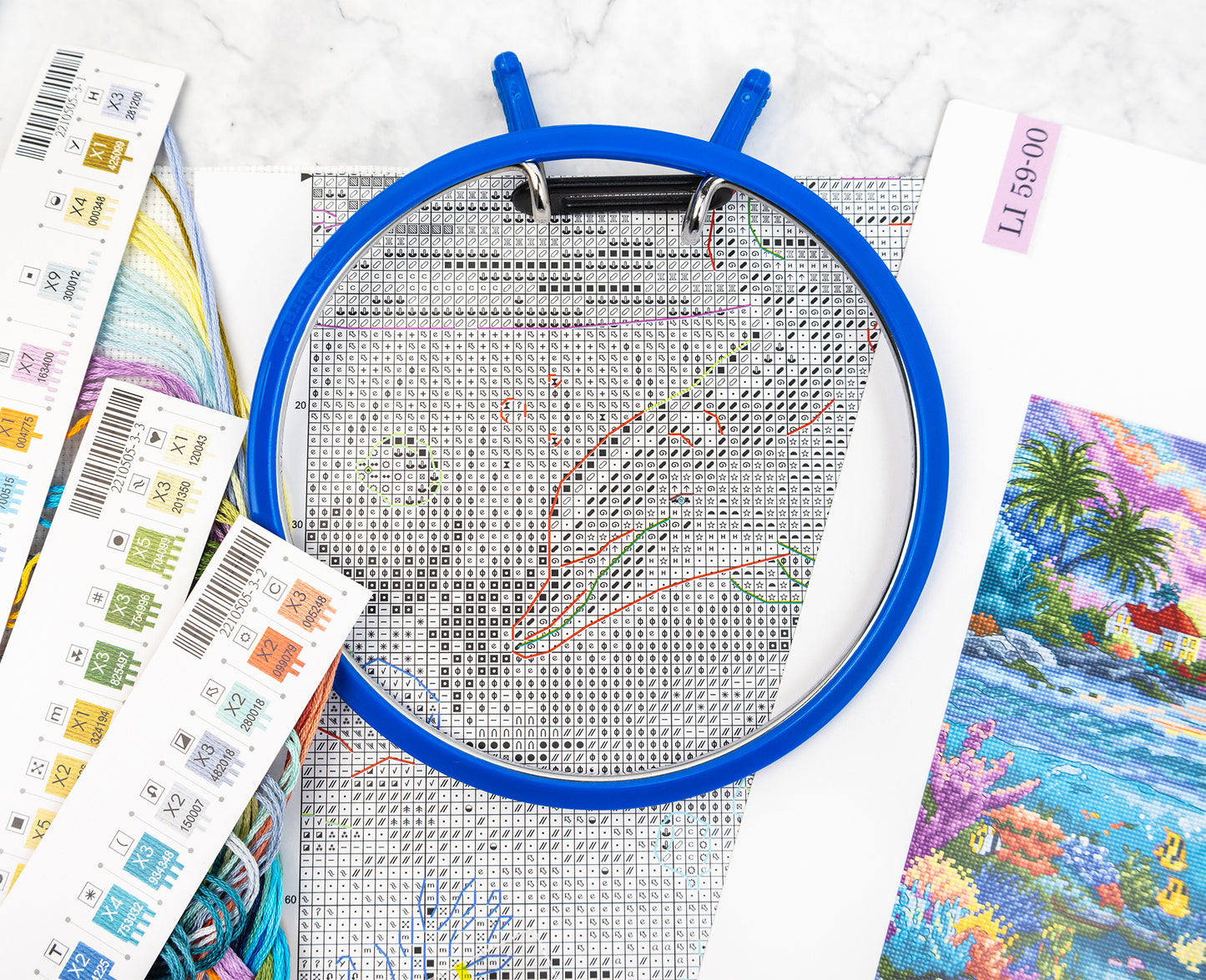 Embroidery hoop with cross-stitch pattern on a white surface with colorful fabric.