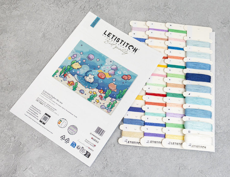 A Letistitch embroidery kit set displayed on a gray textured surface, showing the white instruction booklet with an underwater sea-creature design and a matching card holding multiple colorful thread spools.