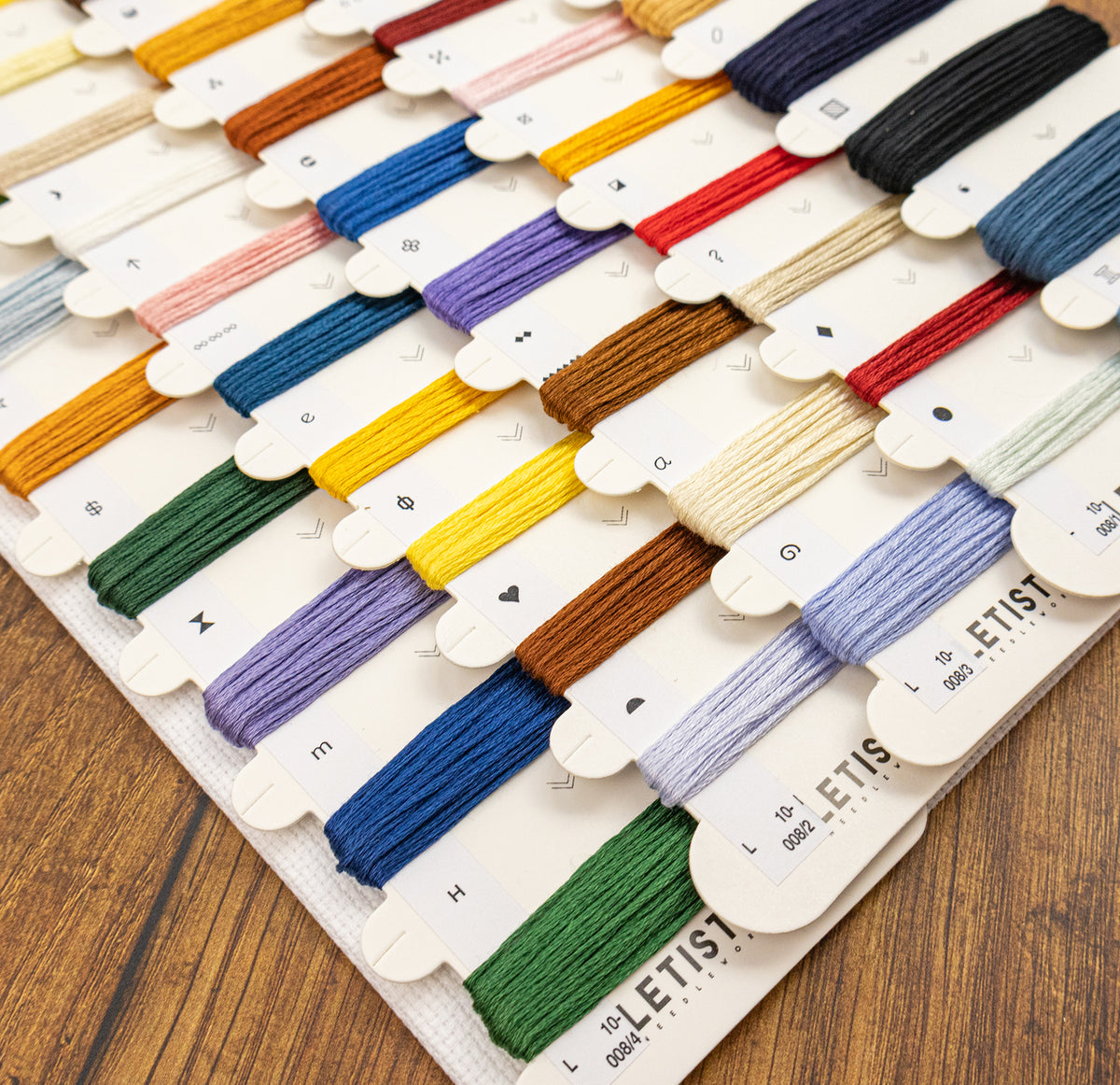 A close-up of a thread sampler card displaying many embroidery floss colors arranged in rows on a wooden surface.