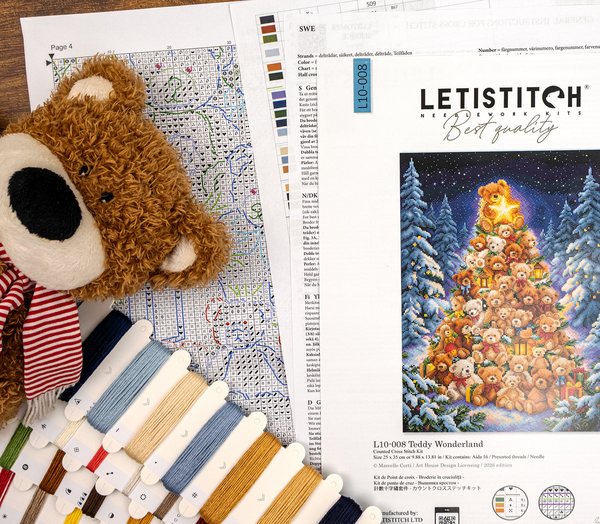Letistitch Needlework 'Teddy Wonderland' embroidery kit pages and materials arranged on a wooden surface, including a teddy bear plush, color swatches, thread cones, and an embroidery pattern sheet showing a decorated Christmas tree made of teddy bears.