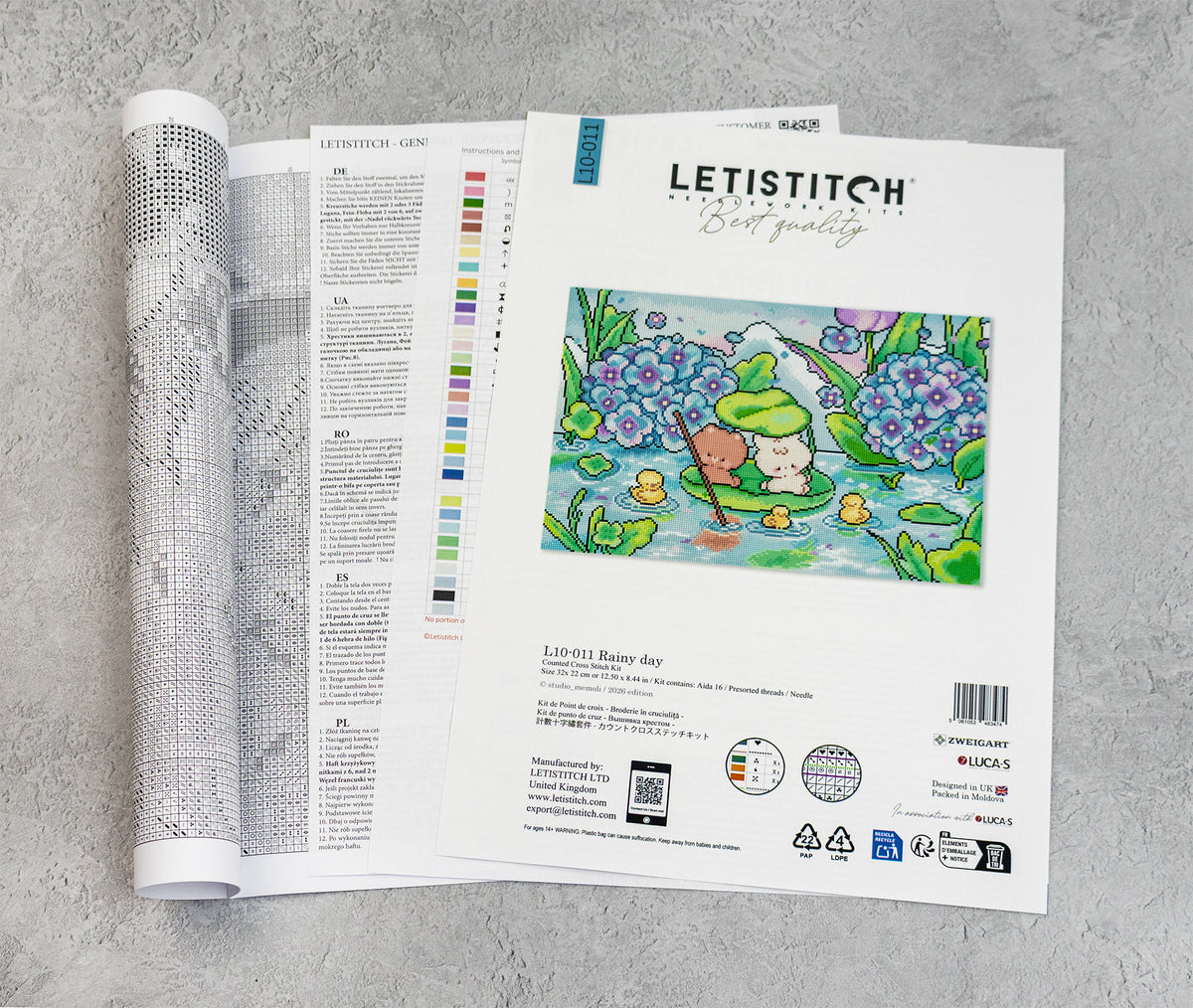 An open craft kit from Letistitch lies on a light gray textured surface, showing the printed pattern pages and a color chart.