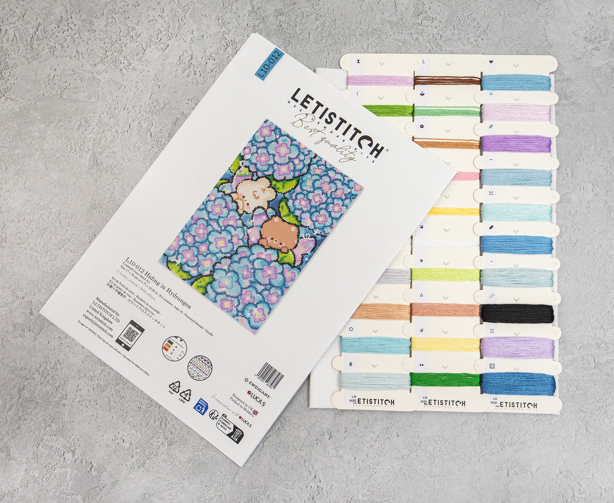 Letistitch Cross Stitch kit packaging shown next to a display card of various colored thread spools on a gray textured background.