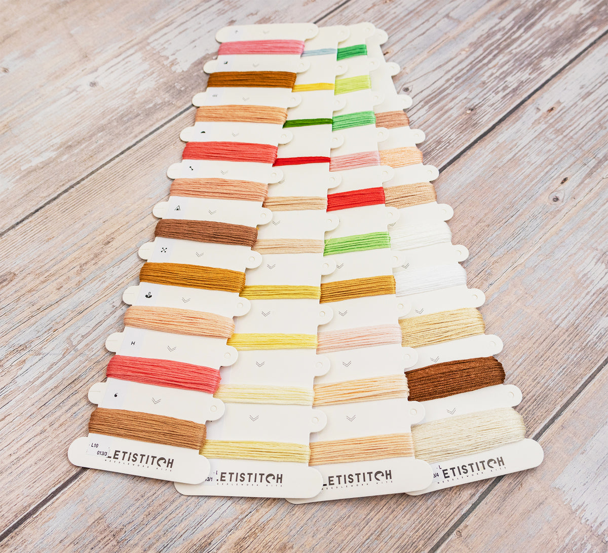 A set of embroidery floss thread spools arranged in rows on a light wood surface. The white cards at the bottom are labeled 'LETISTITCH'.