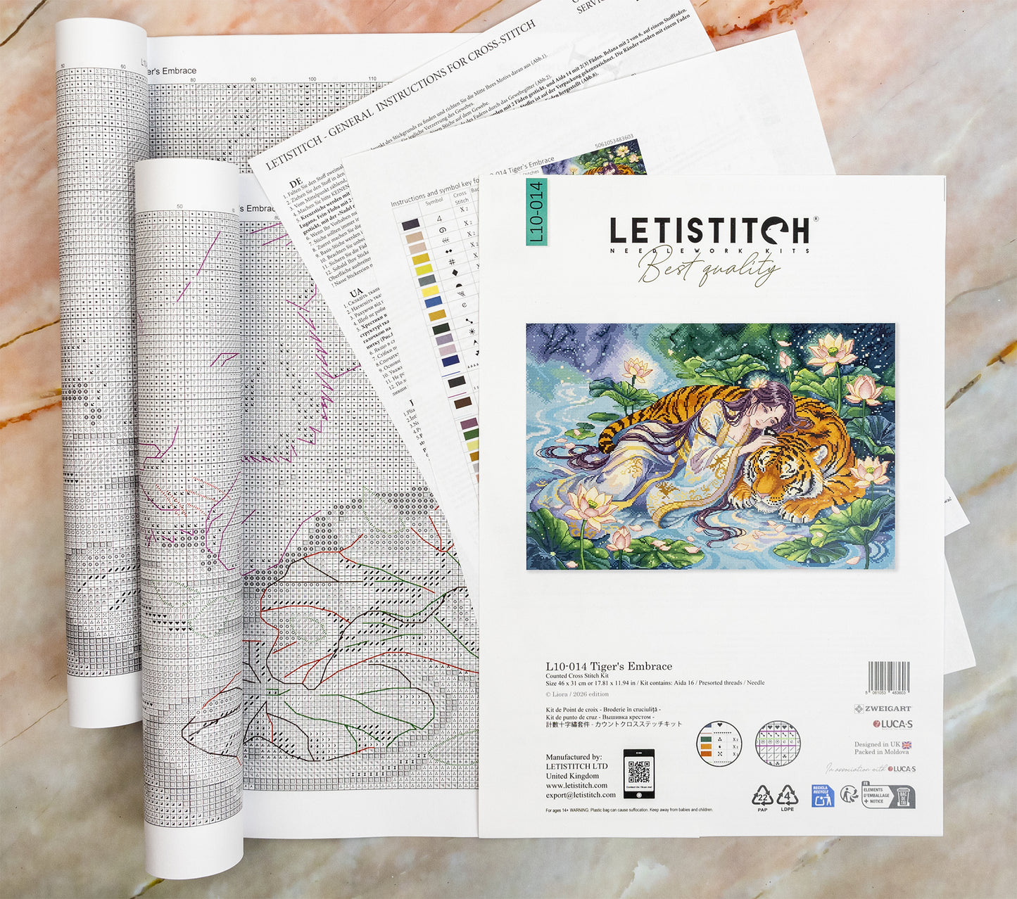 A set of Letistitch embroidery pattern manuals and a finished sample patch showing 'Tiger's Embrace' by artist LIORA VEYNE, arranged on a light marble surface.