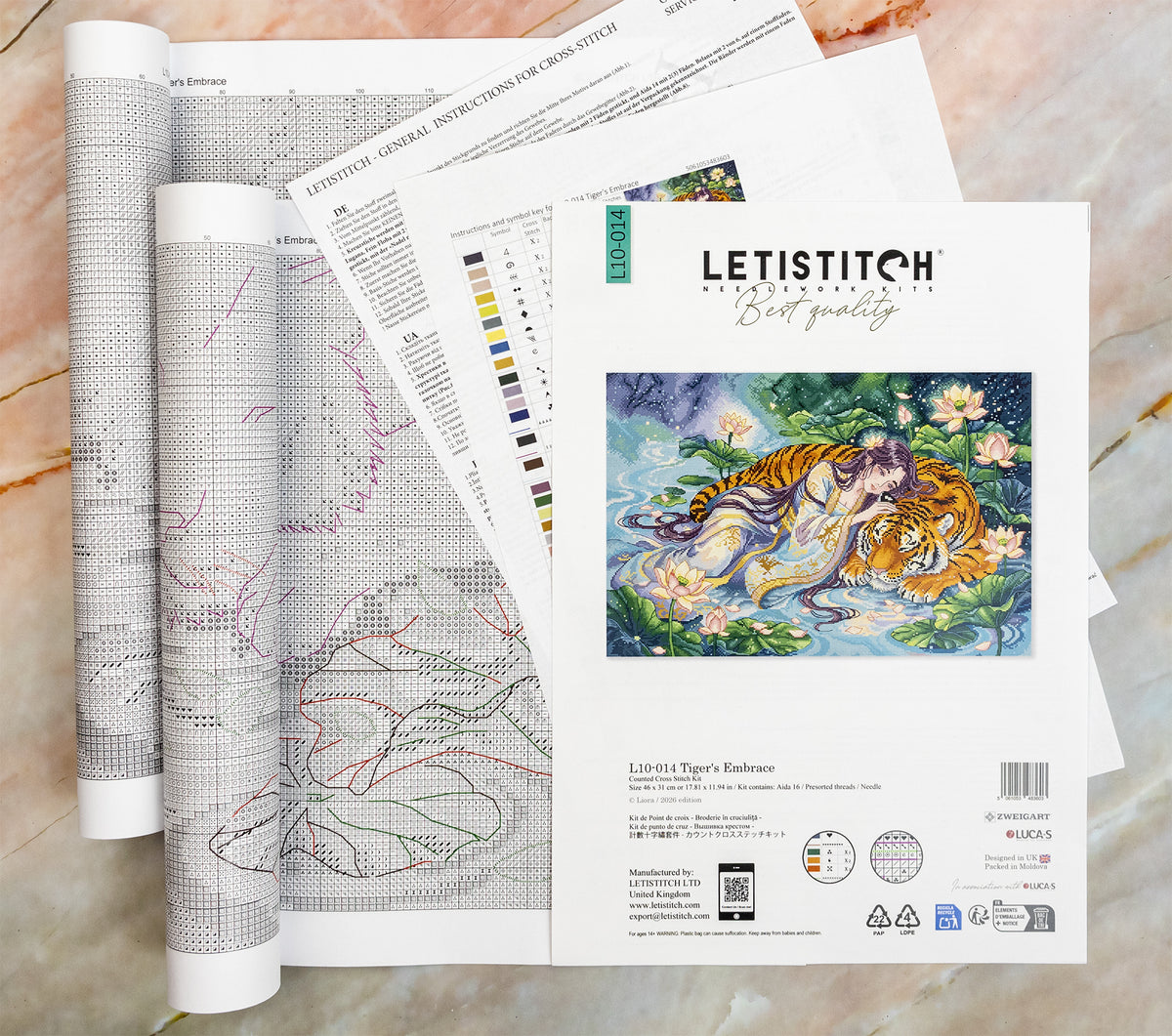 A set of Letistitch embroidery pattern manuals and a finished sample patch showing 'Tiger's Embrace' by artist LIORA VEYNE, arranged on a light marble surface.