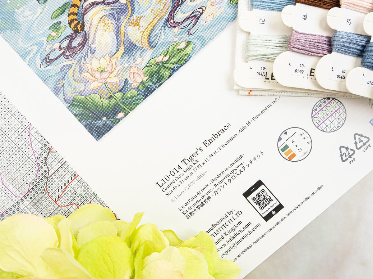A printed embroidery pattern sheet titled 'L10-014 Tiger's Embrace' by LETISTITCH LTD, shown alongside spools of thread and pale green flowers on a light surface. The pattern features an illustrated tiger and lotus motif.