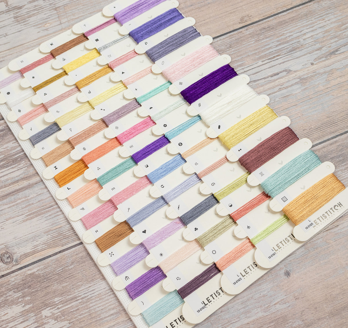 A Letist embroidery floss sampler board displaying multiple rows of colorful thread spools on a light wood background.