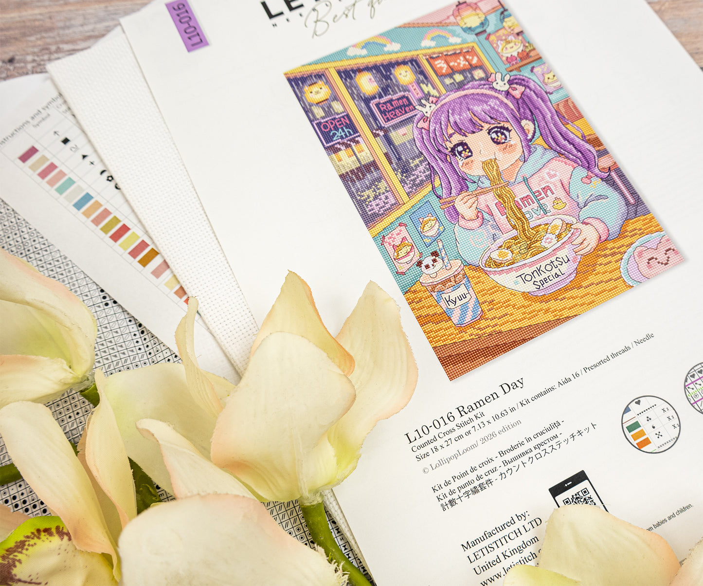 A printed card or art print featuring an illustrated anime-style girl with purple hair eating ramen in a cozy room, styled on top of white envelopes and flowers with Japanese text visible.