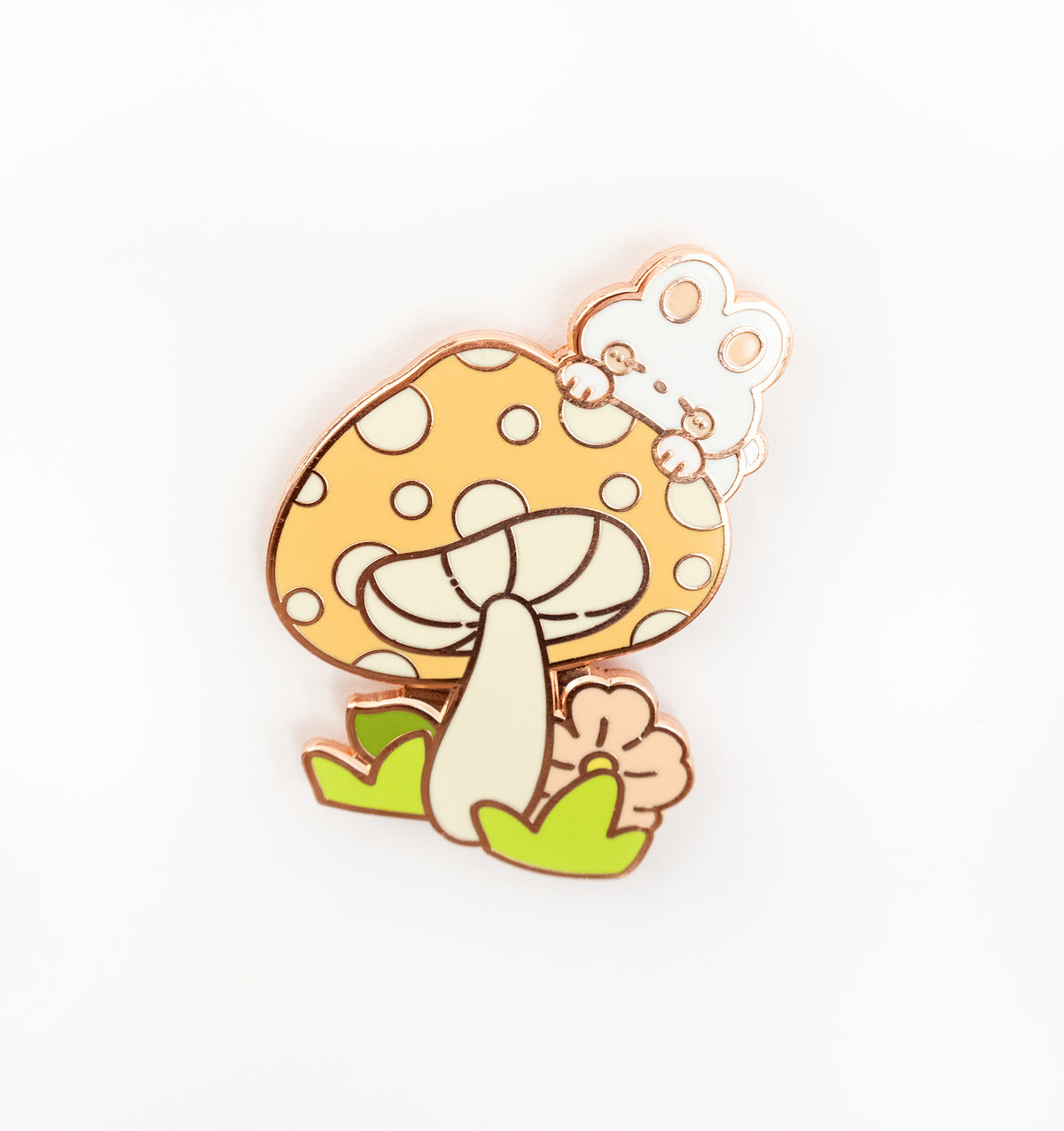 A cute enamel pin featuring a yellow mushroom with white polka dots, a small white bunny peeking from behind it, green leaves at the base, and a rose gold metal outline, shown on a plain white background.