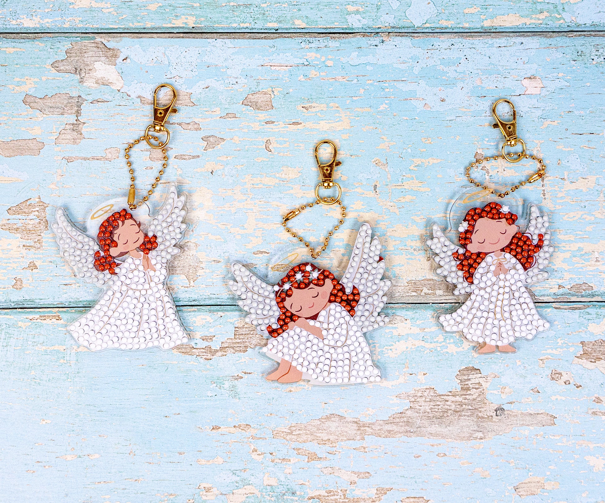 Diamond Dots Three angel keychains with red hair on a wooden surface