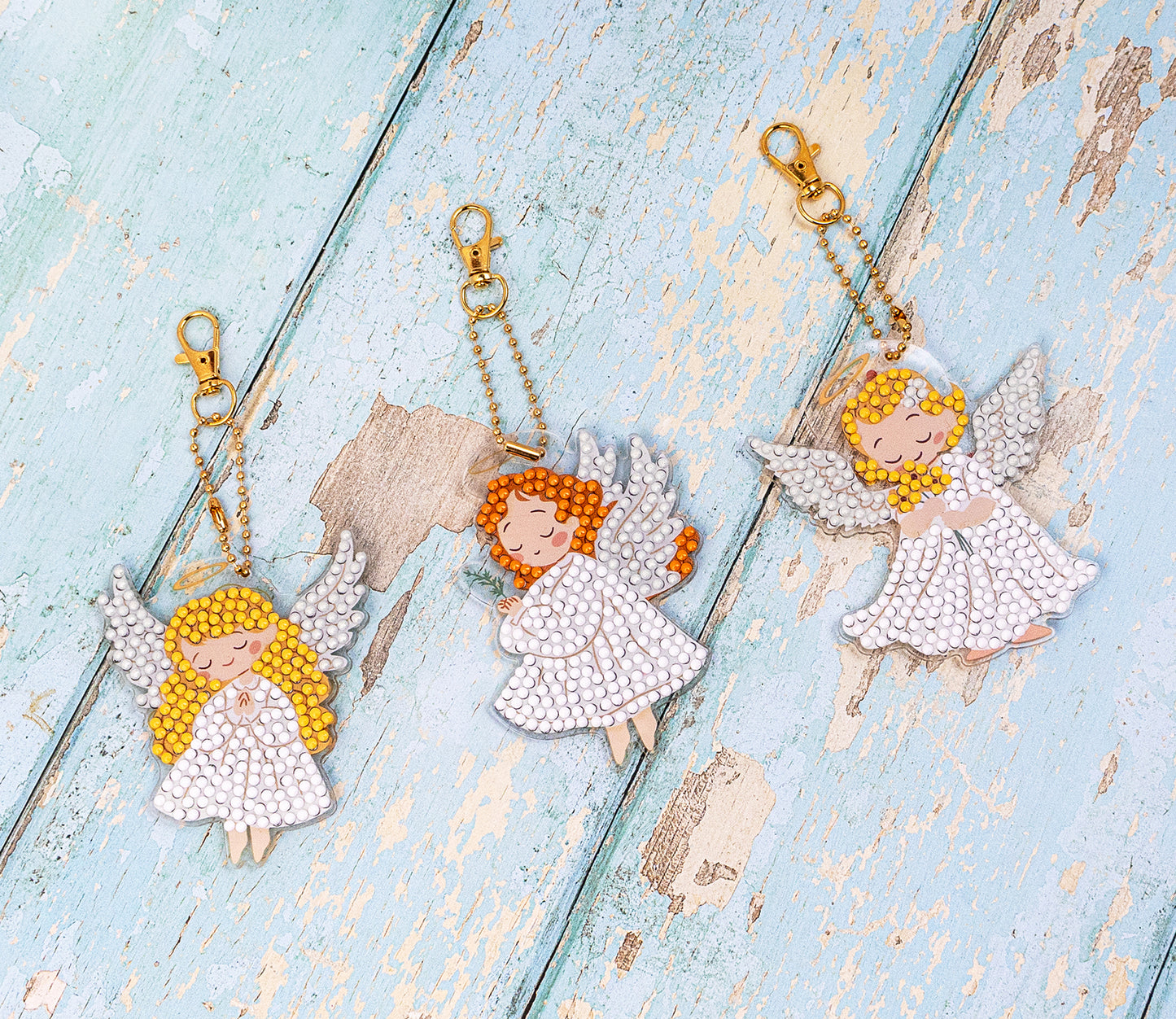 Three angel keychains on a textured blue surface