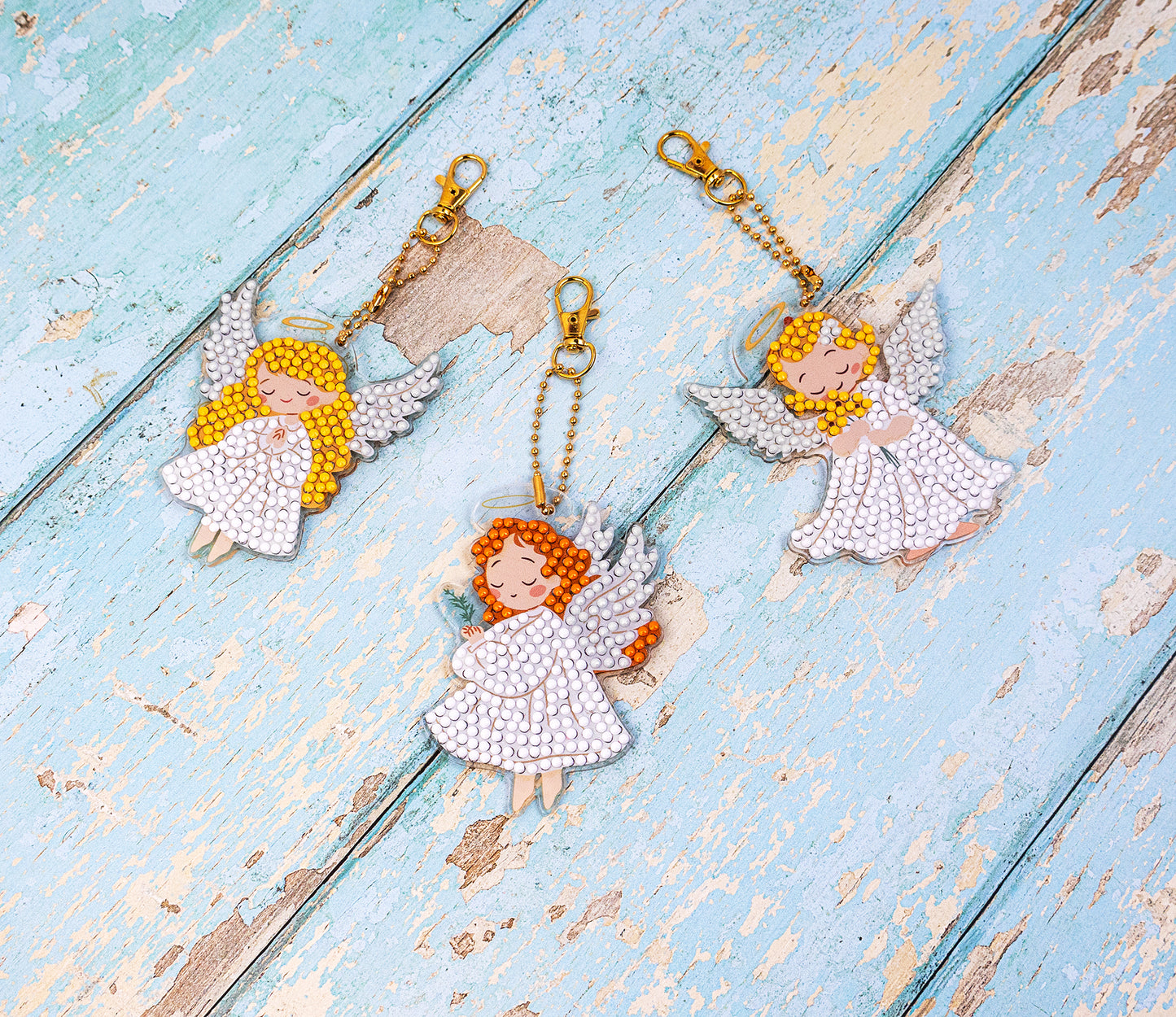 Crystal art Three angel keychains on a textured blue wooden surface