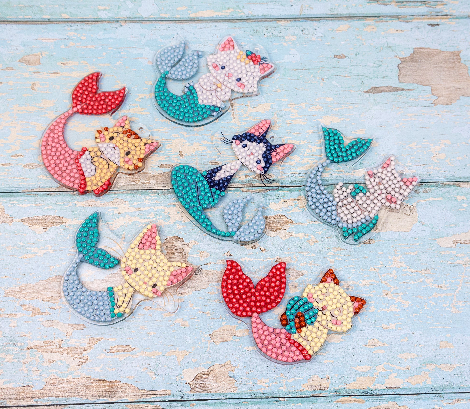 Colorful mermaid-shaped beaded crafts on a light blue wooden surface