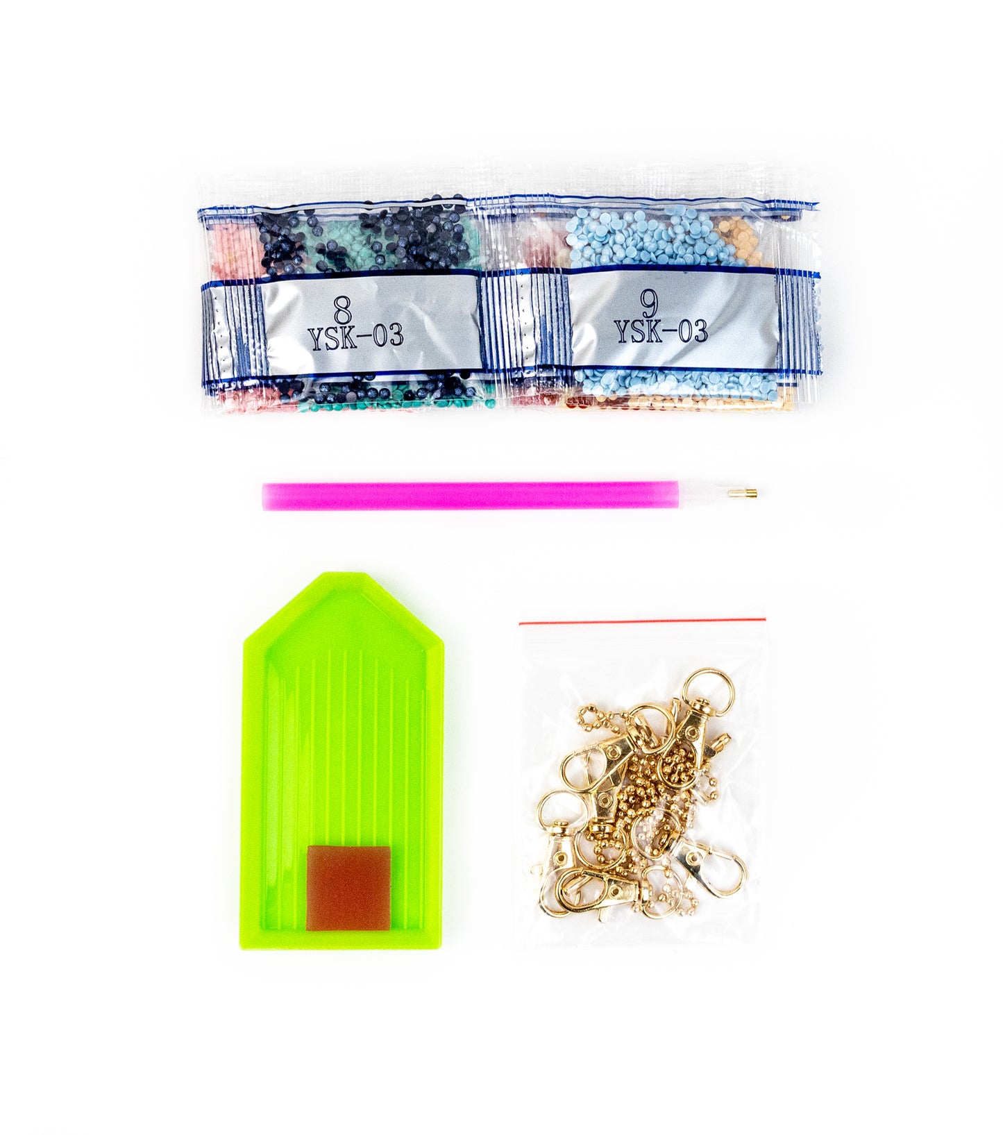 Assorted items including ribbons, a pink pen, a green tag, and gold chains on a white background.