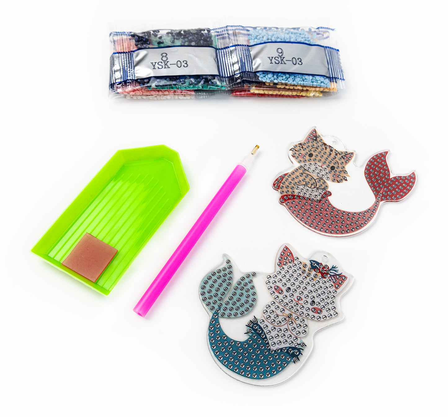 Crafting supplies including a green tool, pink pencil, and decorative cat-shaped items on a white background.