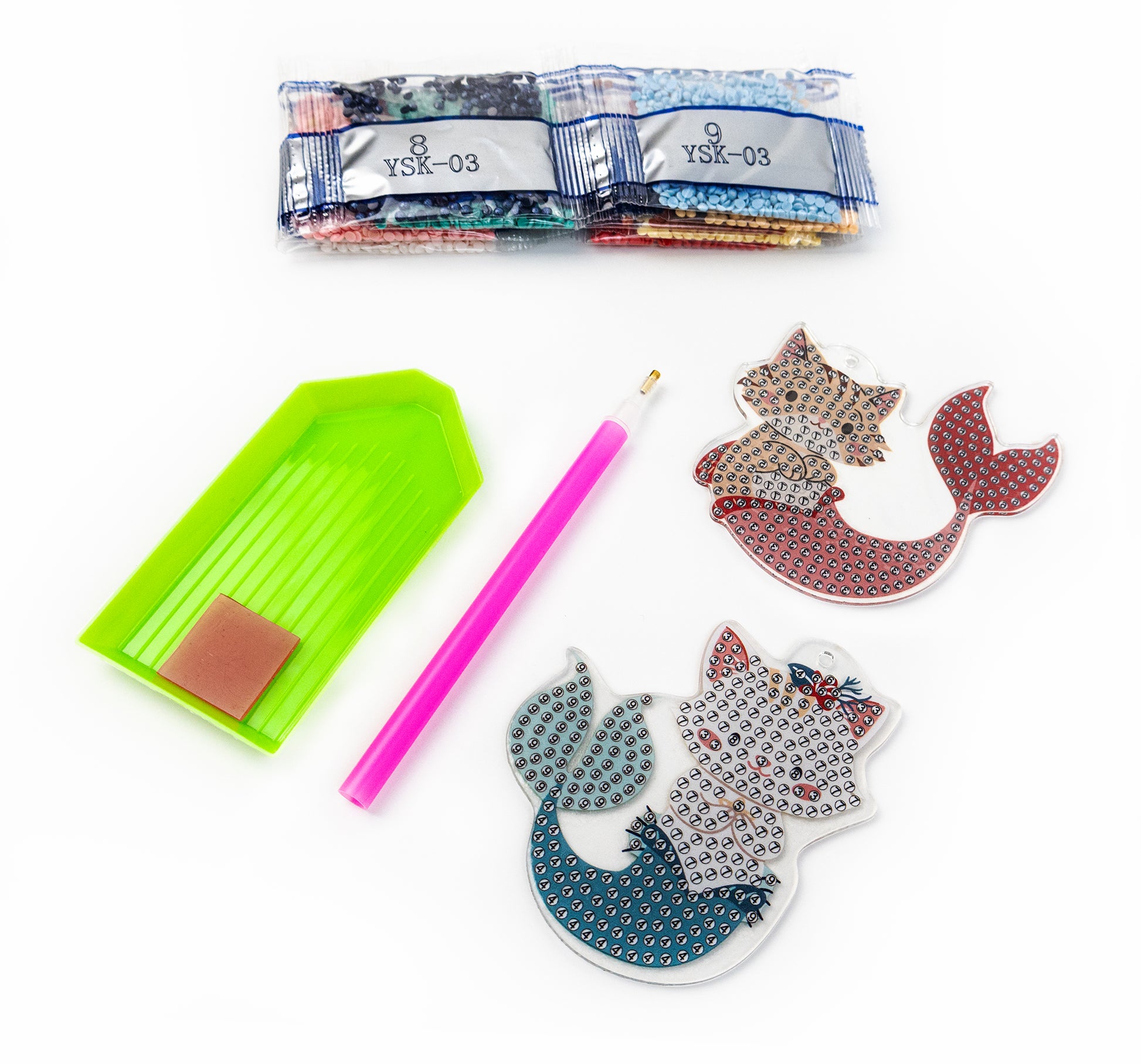 Crafting supplies including a green tool, pink pencil, and decorative cat-shaped items on a white background.