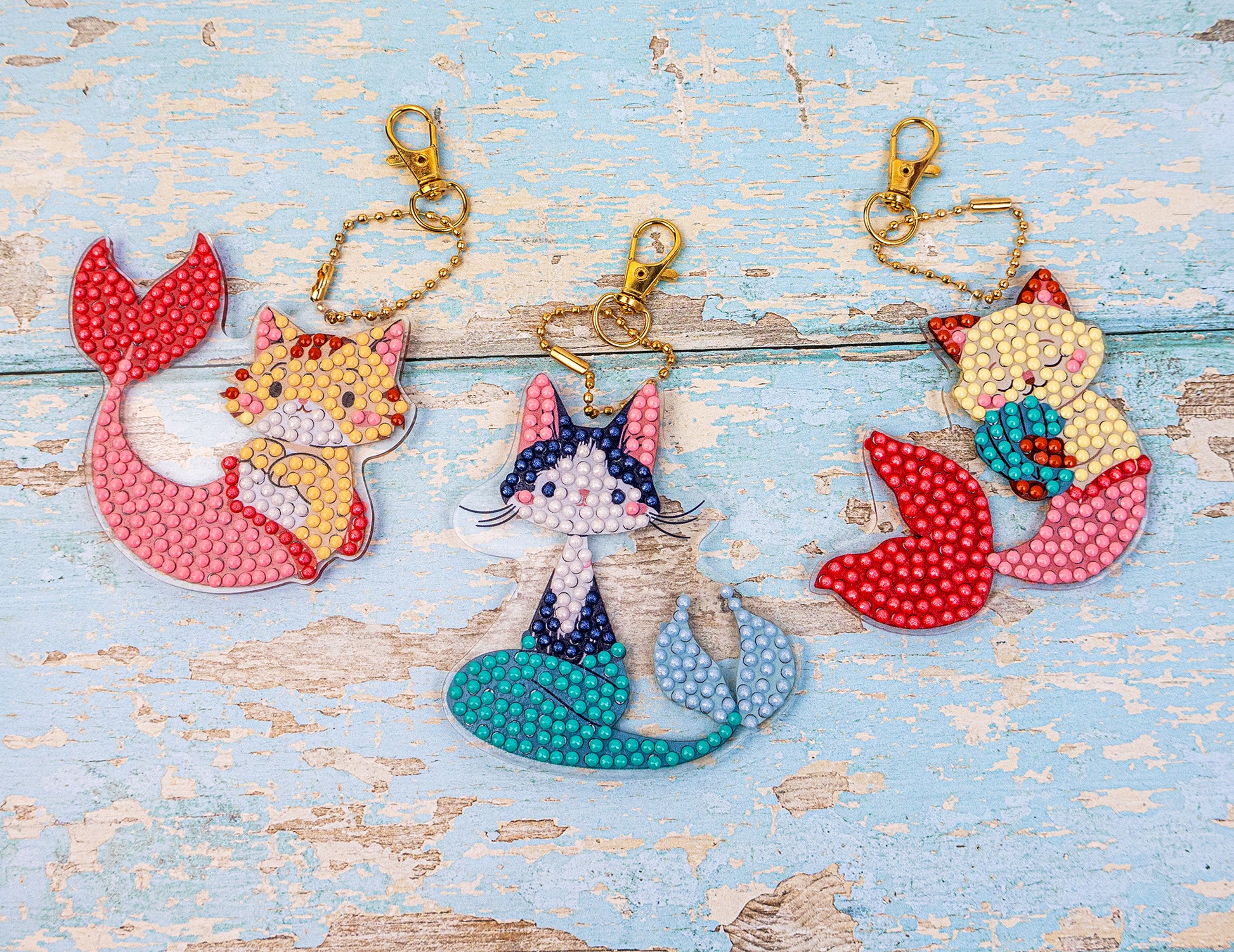 Three colorful keychains with mermaid-themed designs on a wooden surface.