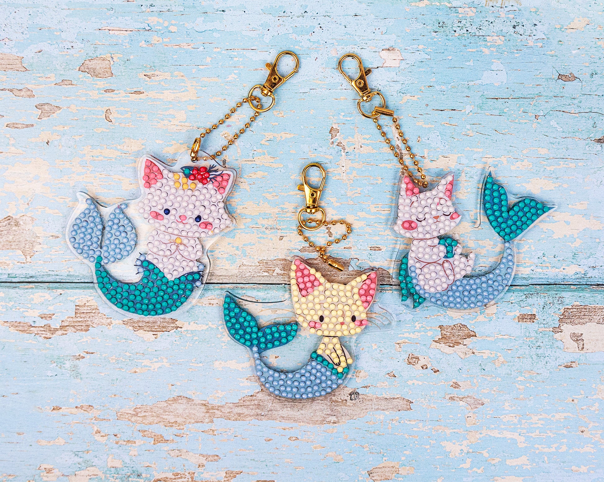 Three cat-themed keychains with mermaid tails on a light blue wooden surface.