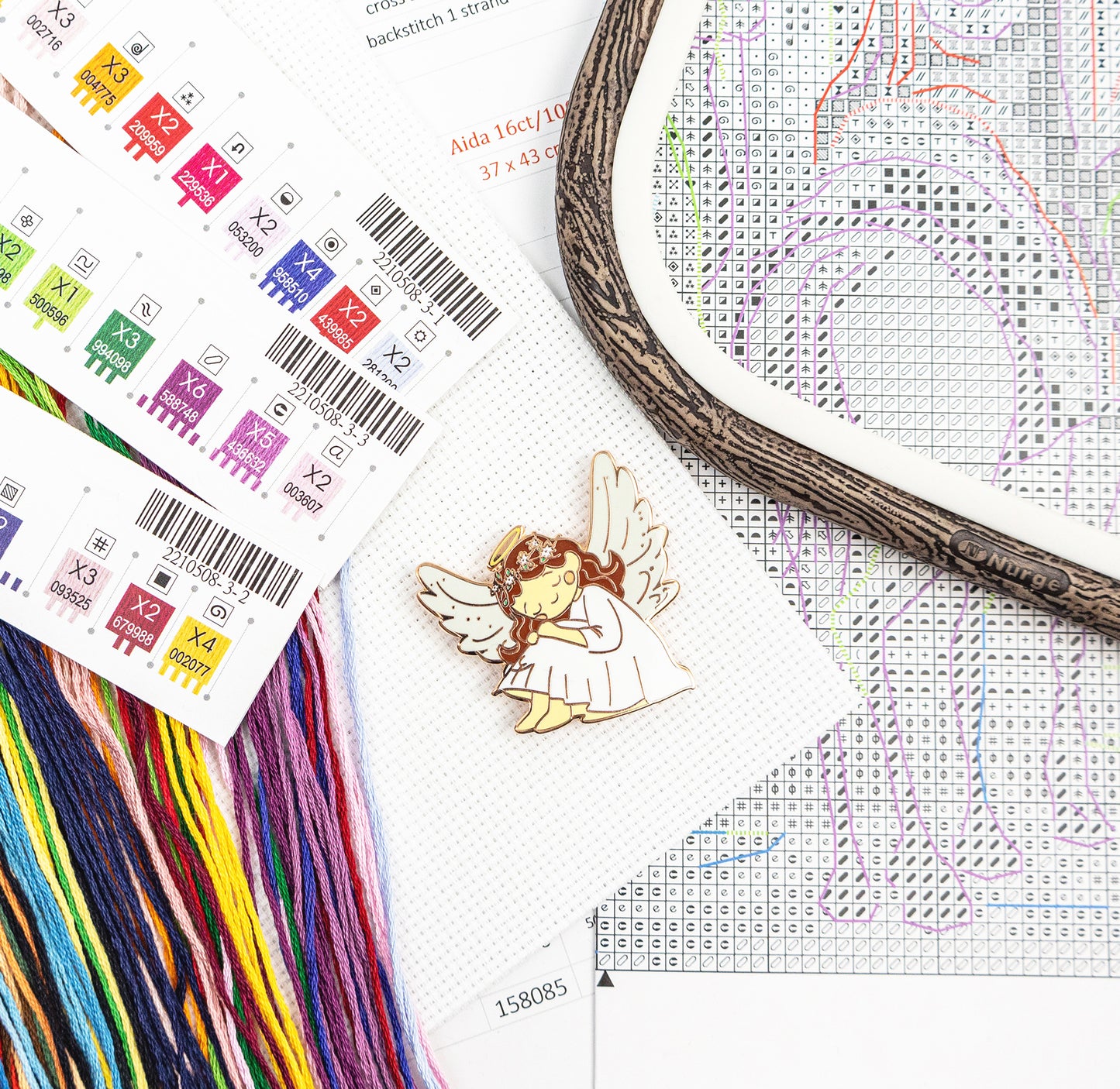 Cross-stitching materials including a hoop, thread, and an angel design on fabric.