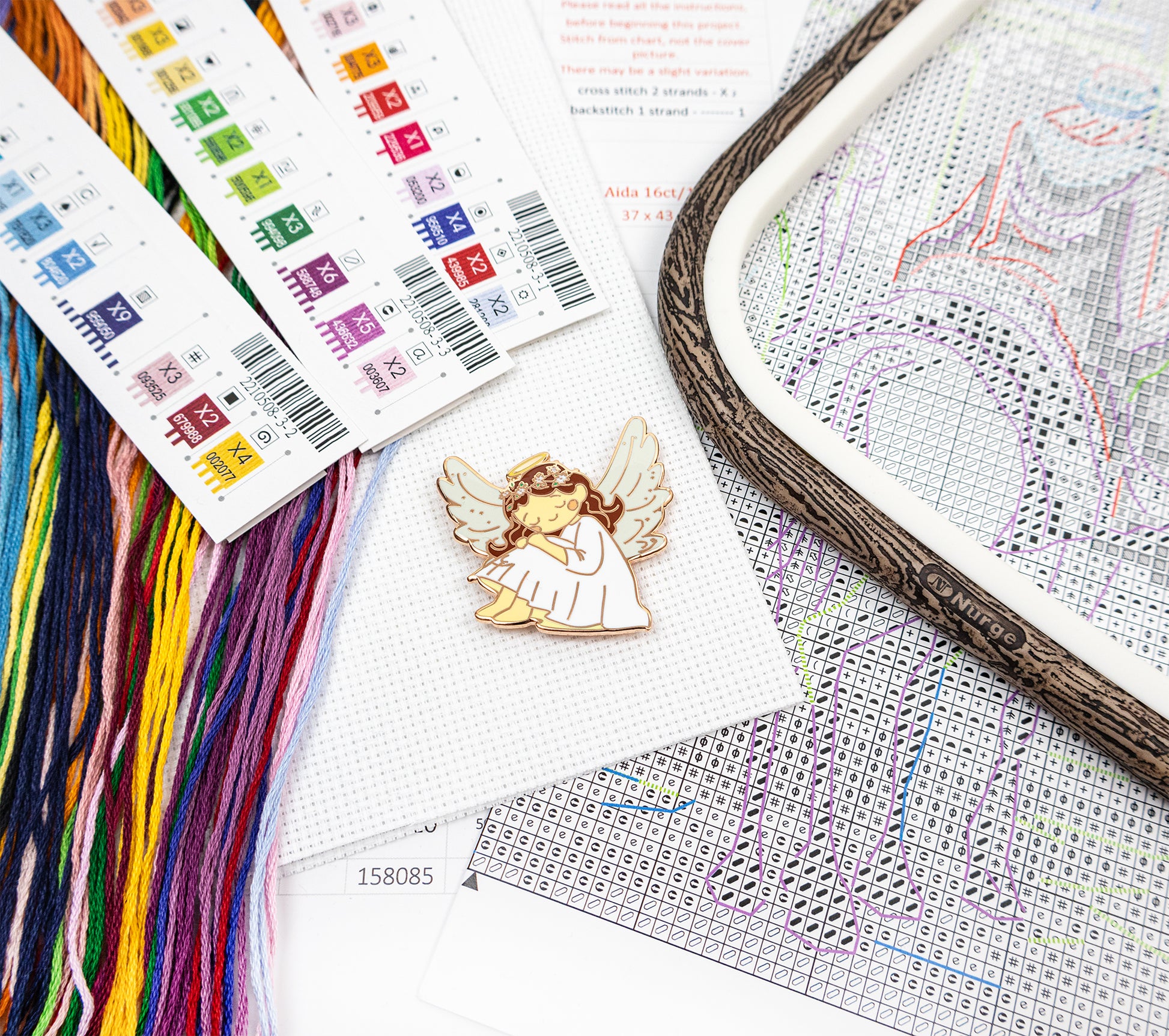 Cross-stitch kit with an angel design, thread, and pattern paper on a white background
