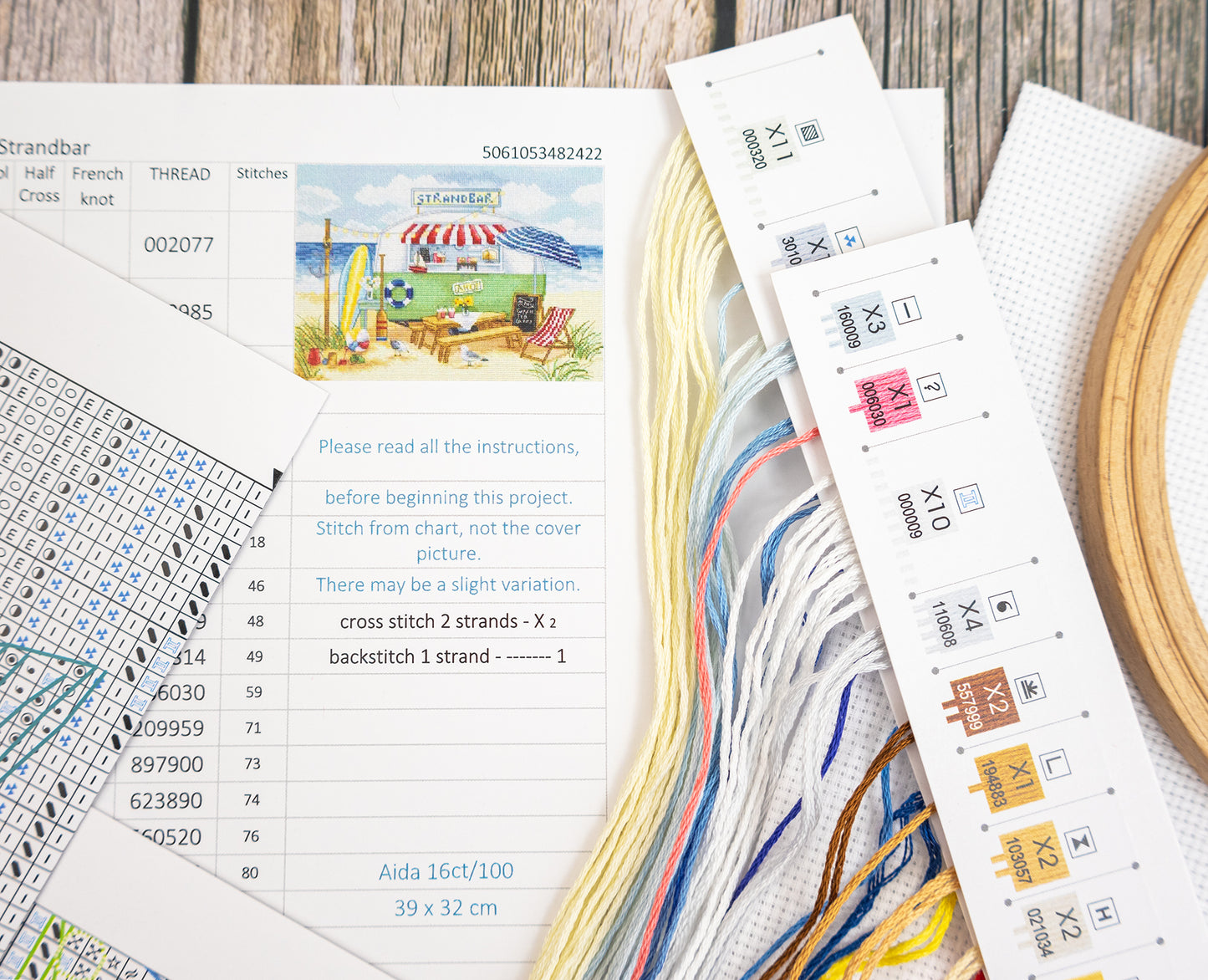 Cross stitch kit with pattern chart, thread, and hoop on a wooden surface