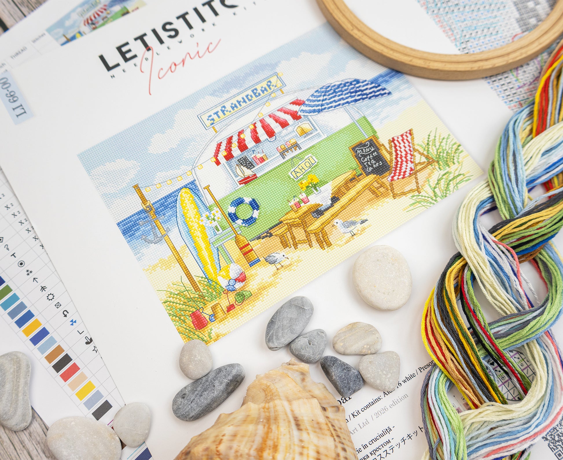 Color swatch book with a beach scene illustration, yarn skeins, stones, and shells on a textured surface.