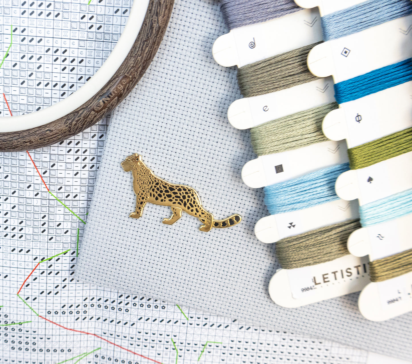 Embroidery hoop with a leopard design pin, cross-stitch chart, and Letistis embroidery threads.