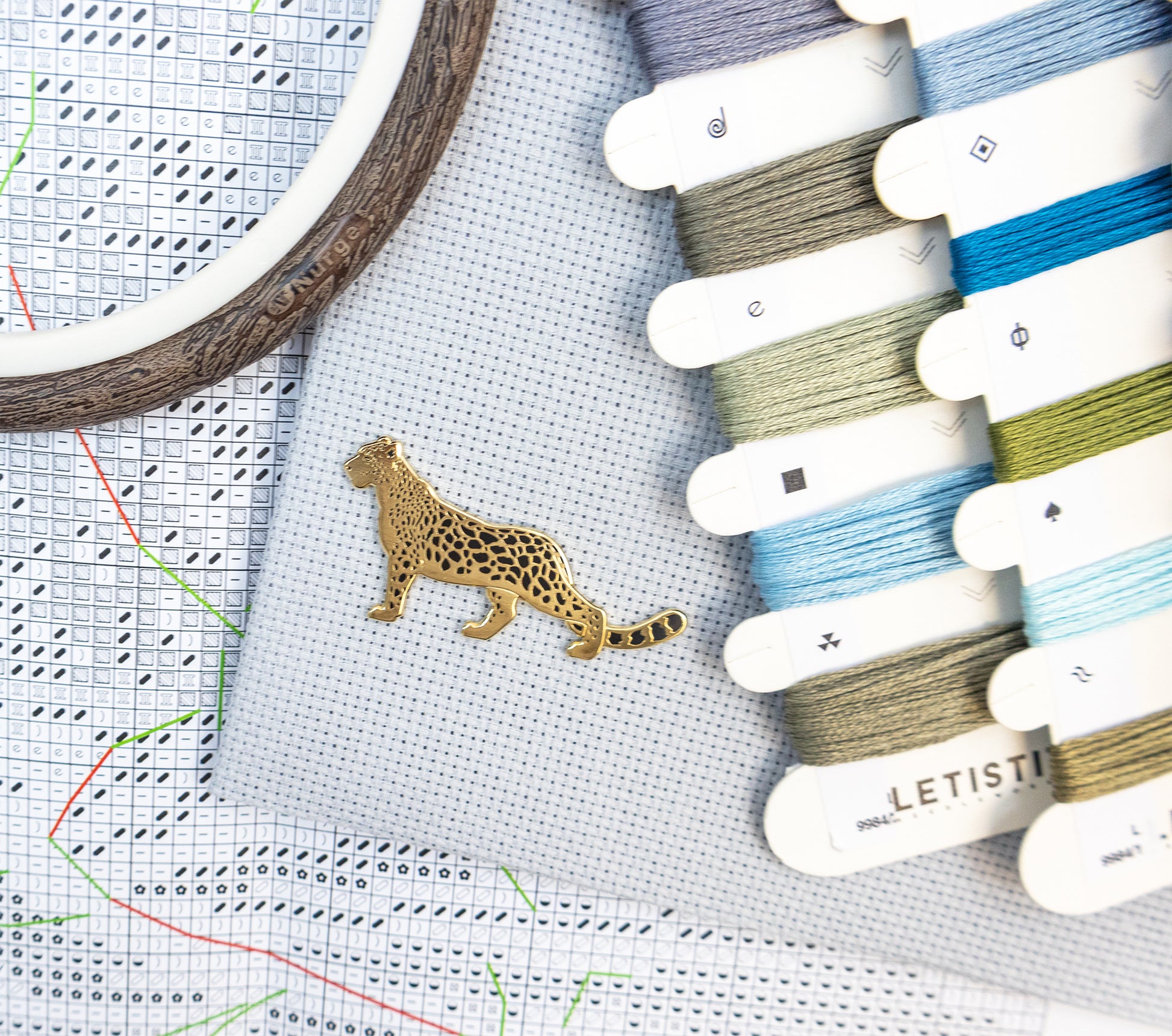 Embroidery hoop with a leopard design pin, cross-stitch chart, and Letistis embroidery threads.
