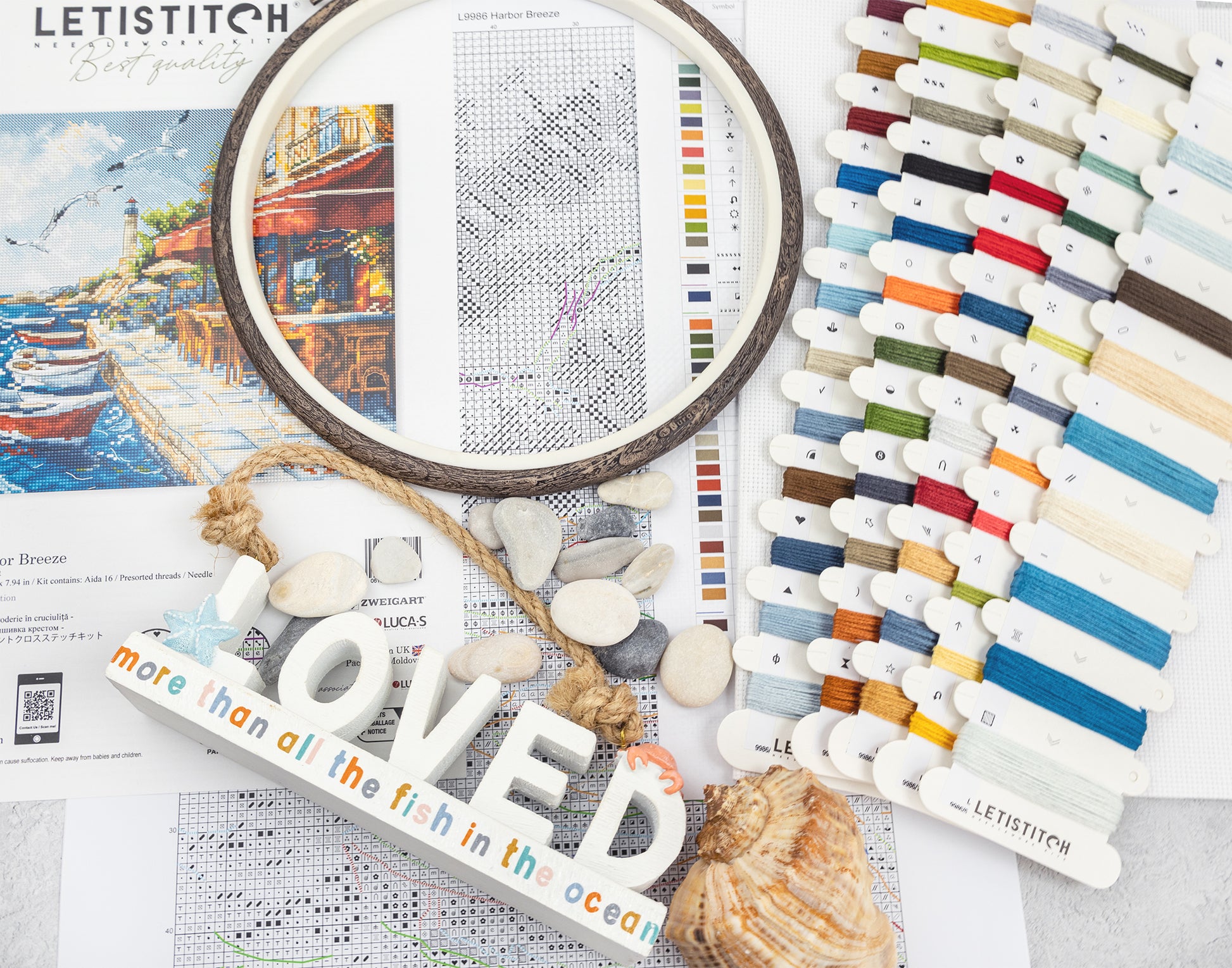 Embroidery hoop, cross-stitch pattern, thread colors, and decorative elements on a table.