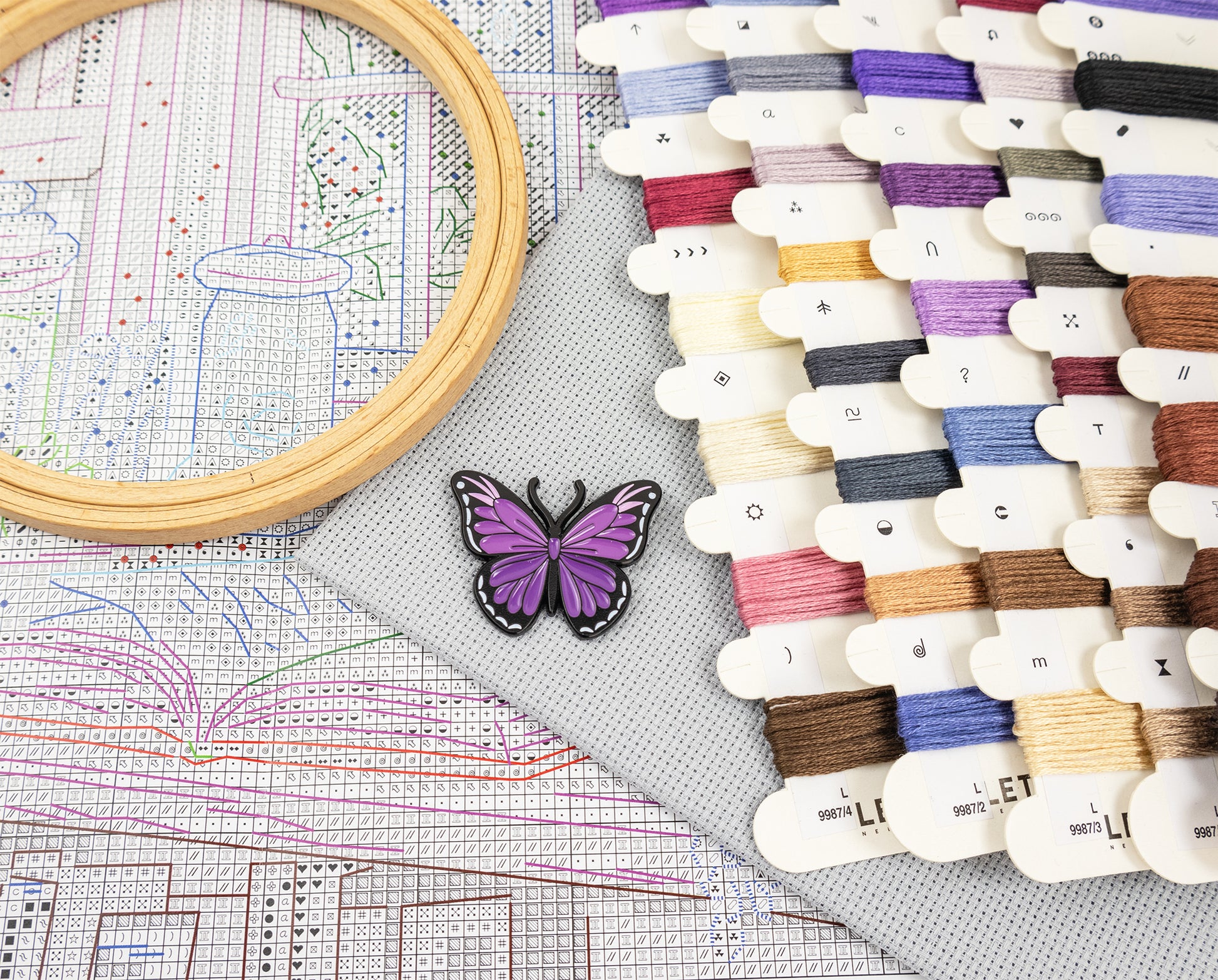 Embroidery hoop, cross-stitch pattern, and spools of thread on a table.
