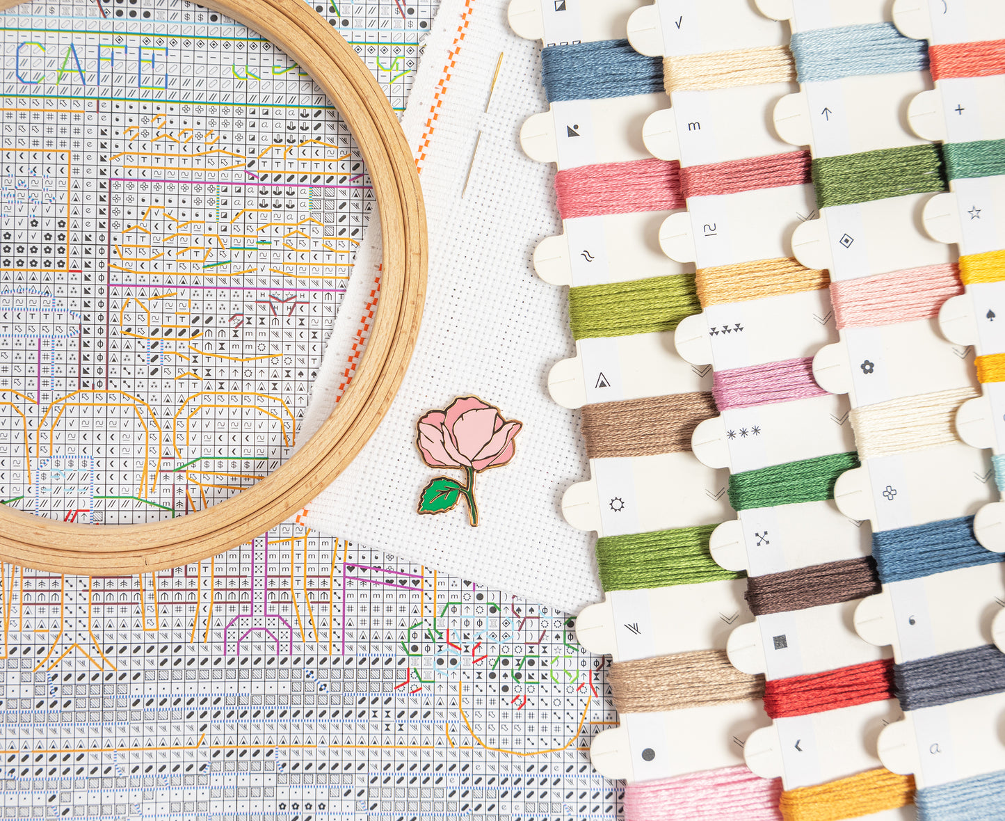 Embroidery hoop with cross-stitched design and thread spools on a white background