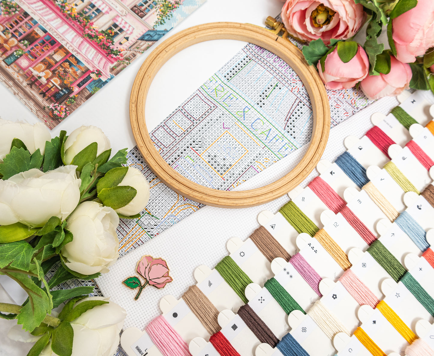 Cross-stitching project with embroidery hoop, threads, and flowers on a table.
