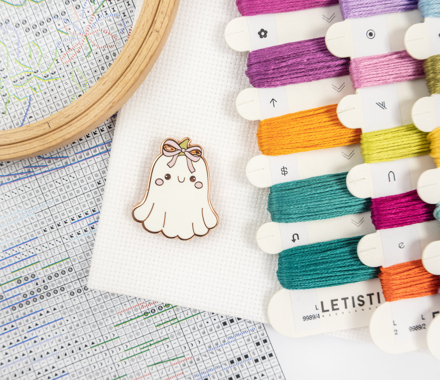 Embroidery hoop with colorful threads and a cute ghost pin on a cross-stitch chart.