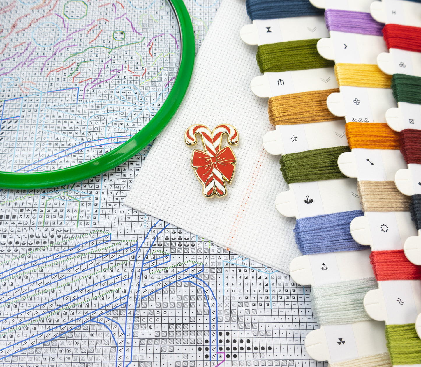 Cross-stitching materials including thread, a design chart, and a candy cane-shaped pin.