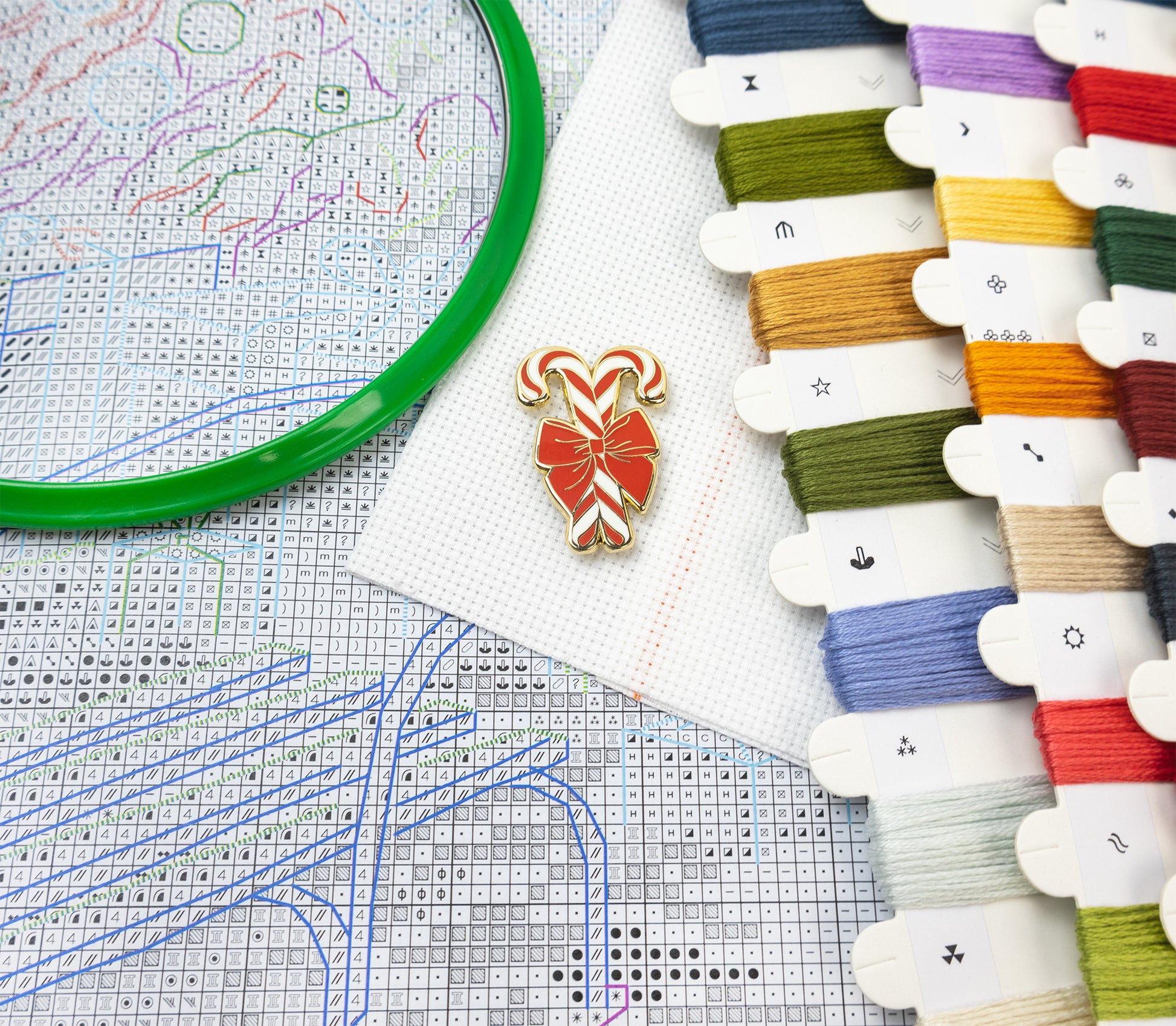 Cross-stitching materials including thread, a design chart, and a candy cane-shaped pin.