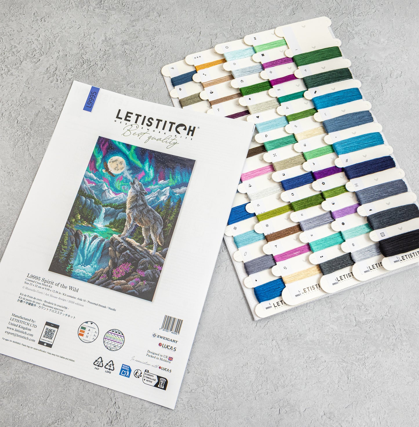 Letistitch embroidery floss set with a printed sample card showing a wolf and aurora design, alongside a large array of colorful thread spools on a light gray textured background.