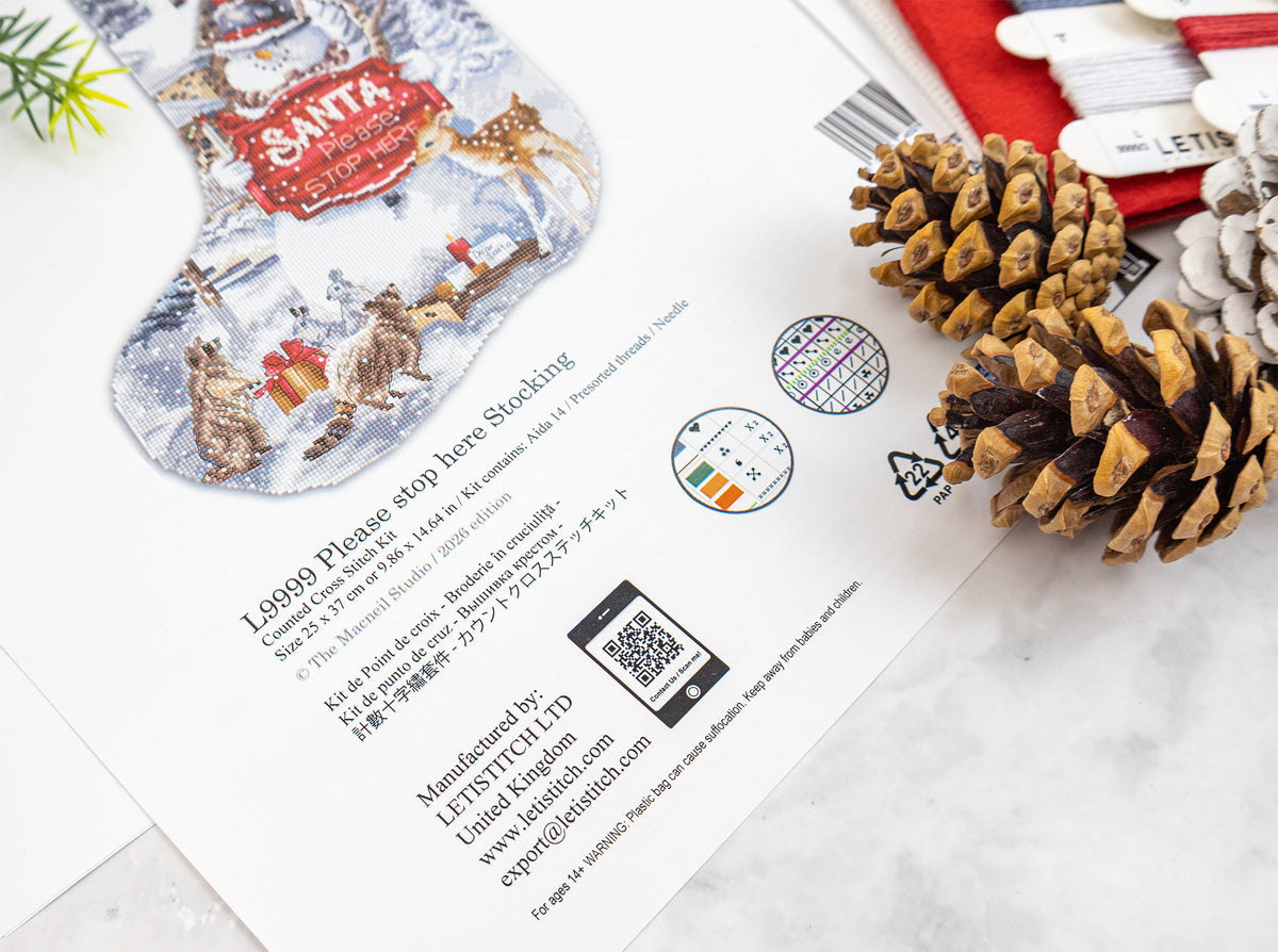 A printed Christmas stocking gift card or shipping label featuring Santa-themed illustrations, placed on a light marble surface with pinecones and red wrapping paper around it.