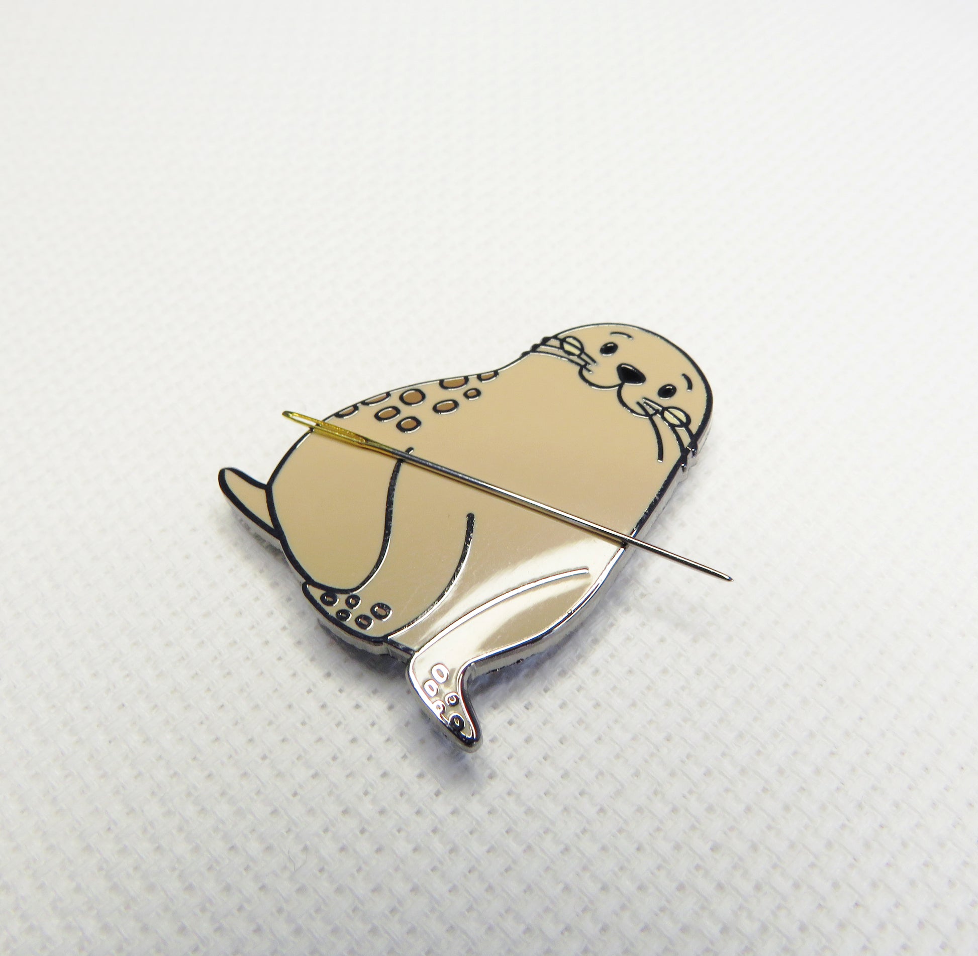 Seal-shaped Needleminder with a needle on a textured white background