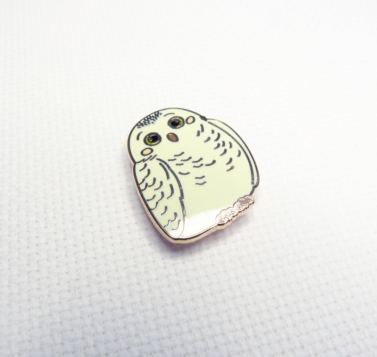 Enamel needleminder of a stylized owl on a textured white background