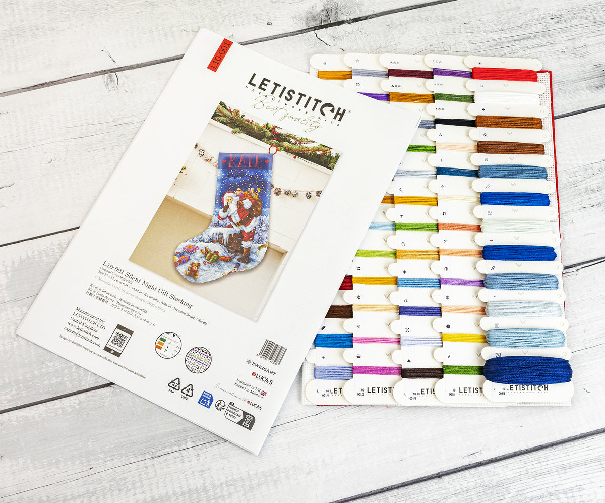 Letistitch Silent Night Gift Stocking kit shown with its printed instruction booklet and a matching thread sampler card on a white wood background.