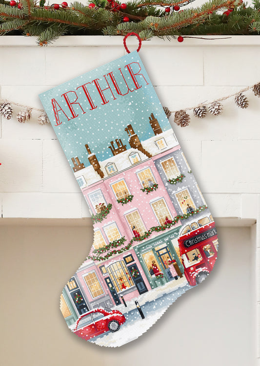 Christmas stocking with a festive design of a town scene, snowflakes, and a red car, hanging on a white wall.