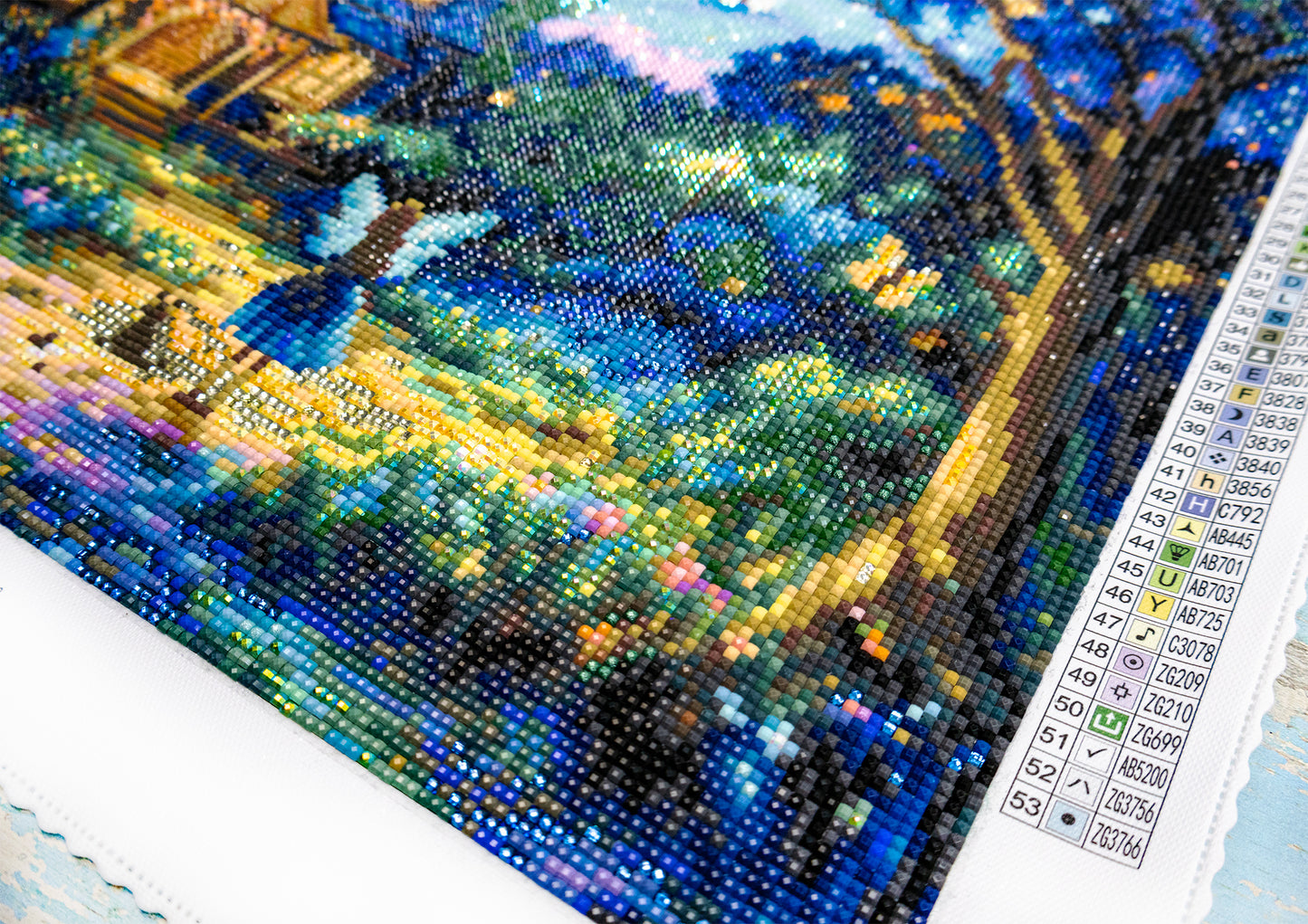 Close-up of a diamond painting project with a computer screen displaying color swatches.