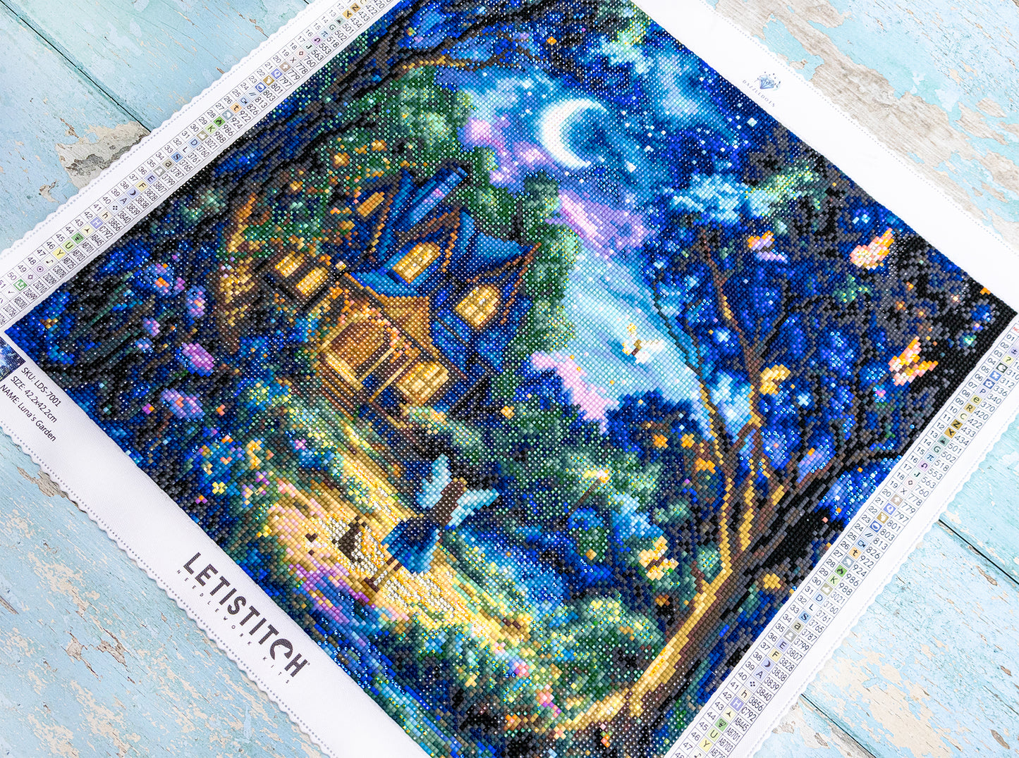 Diamond art with a blue house and moonlit trees on a wooden surface