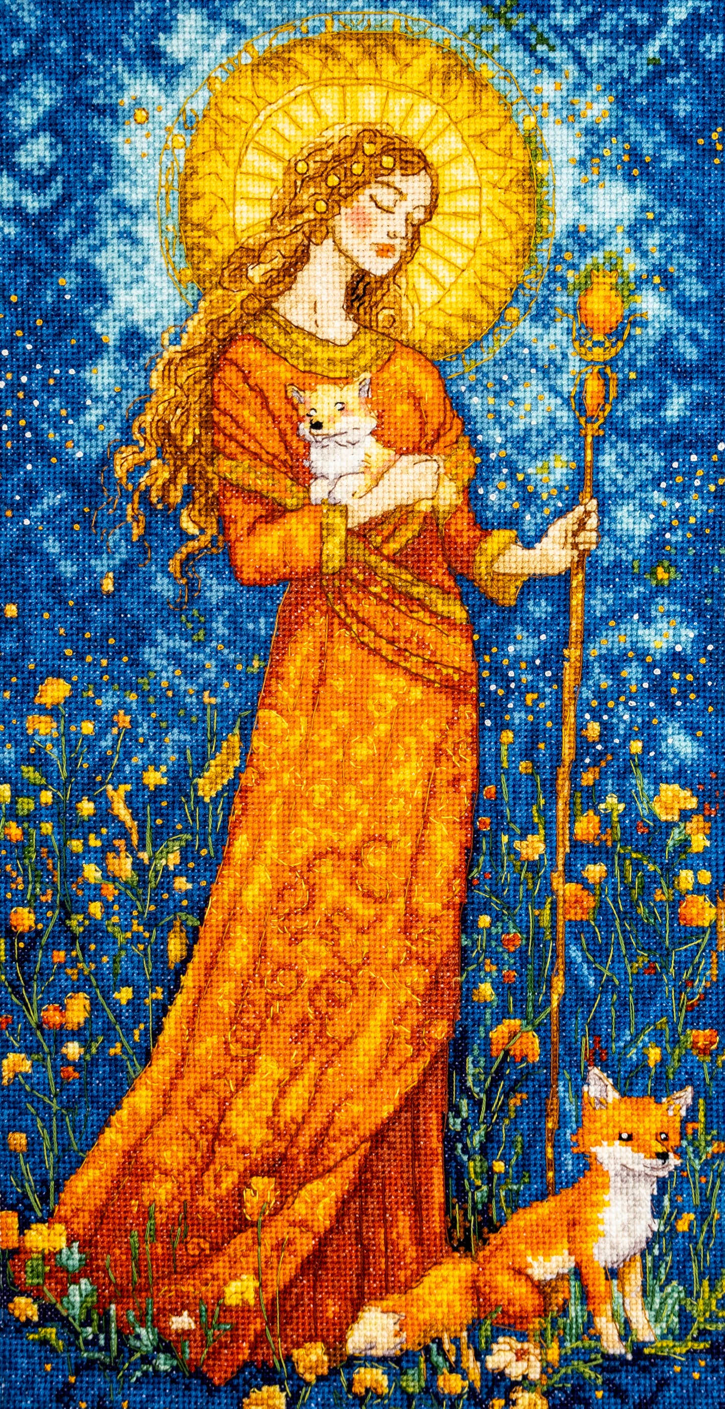Cross-stitched artwork of a woman in an orange robe with a fox, set against a blue sky with stars.