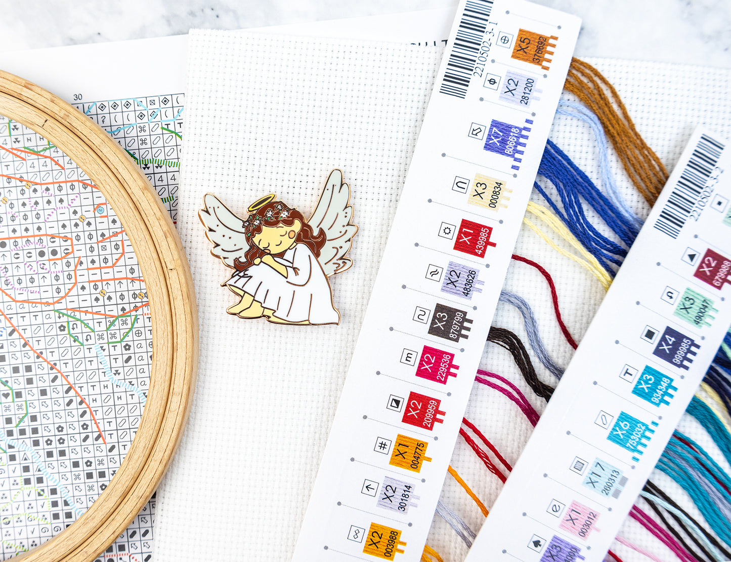 Cross-stitching materials including an embroidery hoop, cross-stitch chart, on a white surface.