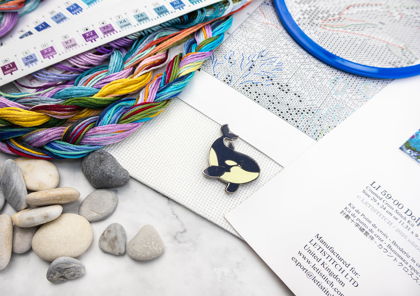 Colorful yarn, stones, and a whale-shaped pendant on a marble surface with a patterned paper.