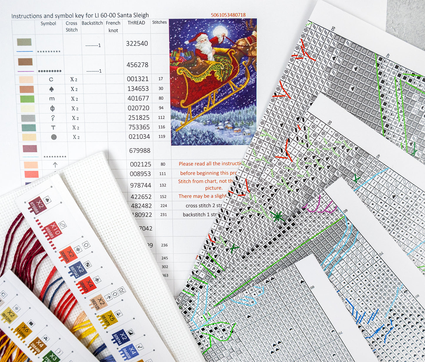 Cross-stitch pattern sheets with a Santa Claus sleigh design on a textured surface.